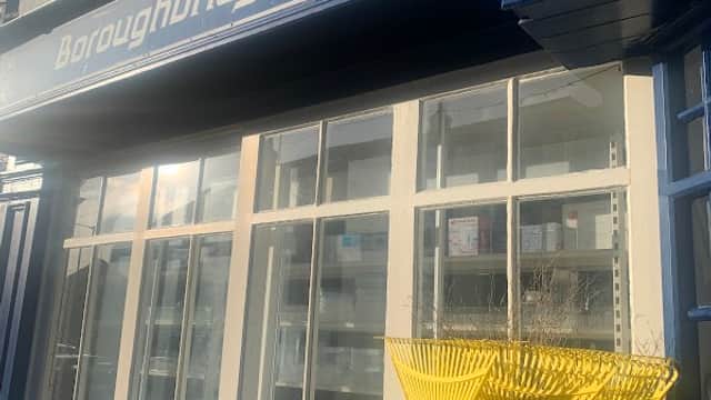 Sign for Boroughbridge Hardware Ltd with blue facade and yellow garden rakes displayed outside the window.