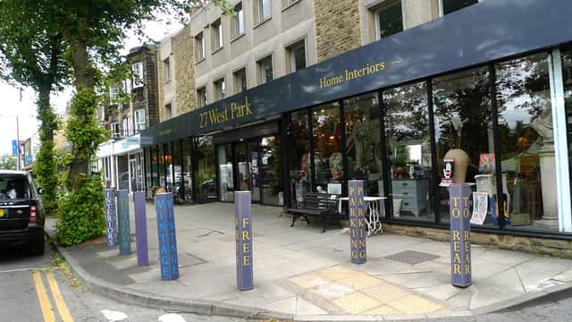 "Shopfront of 27 West Park Antiques & Home Interiors with bold signage, parking signs, and greenery lining the street."