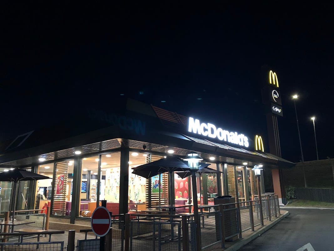 McDonald's restaurant at night, featuring outdoor seating, bright signage, and illuminated interior.