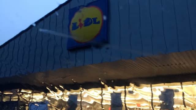 Lidl storefront with illuminated interior, seen through rain-streaked glass in a twilight setting.