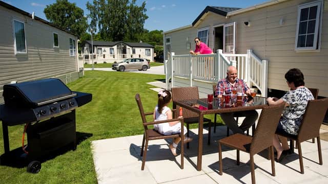 A family enjoying drinks at a patio table near a grill, with holiday homes and green lawns in the background.