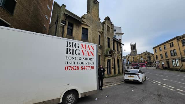 Kingsgate Parking area with a logistics van, historic buildings, and a church tower in Huddersfield, Yorkshire.