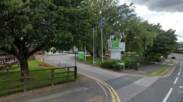 Entrance to Holiday Inn with green signage, trees, and parked cars along a quiet road in Alverthorpe, Yorkshire.