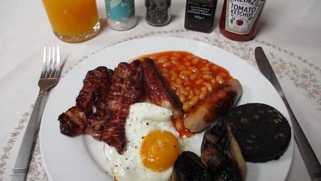 A hearty breakfast plate with bacon, sausages, baked beans, a fried egg, black pudding, and mushrooms, alongside sauces.