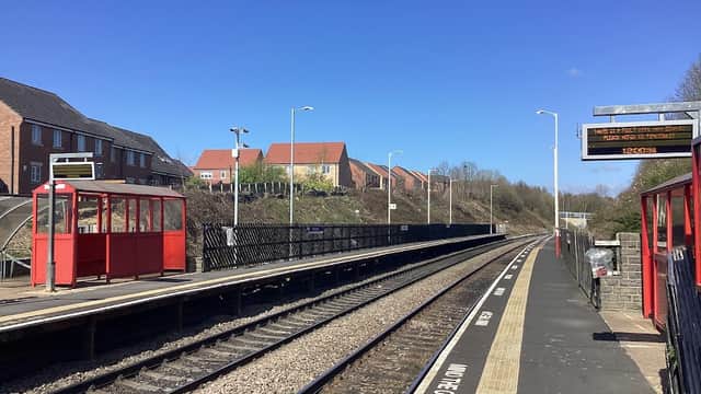 Railway station platform in Cottingley, Yorkshire, with red shelters, track, and residential buildings in the background.