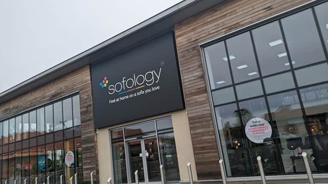 Modern furniture shop with large glass windows and a wooden facade, featuring a prominent sign for Sofology.