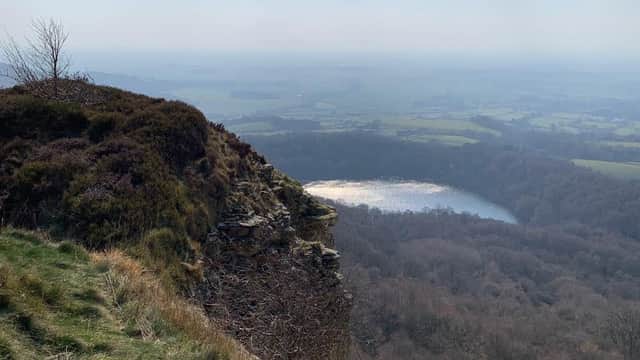 Scenic view from Kilburn Forest Car Park, overlooking a lake surrounded by trees and rolling hills under a hazy sky.
