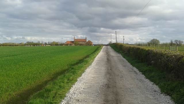 Gravel road leading to Park Farm, surrounded by green fields under a cloudy sky in Scorborough, Yorkshire.