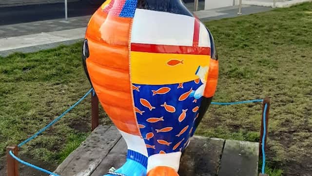 Colorful puffin statue with fish patterns, situated on grass near a pathway and buildings in Bridlington, Yorkshire.