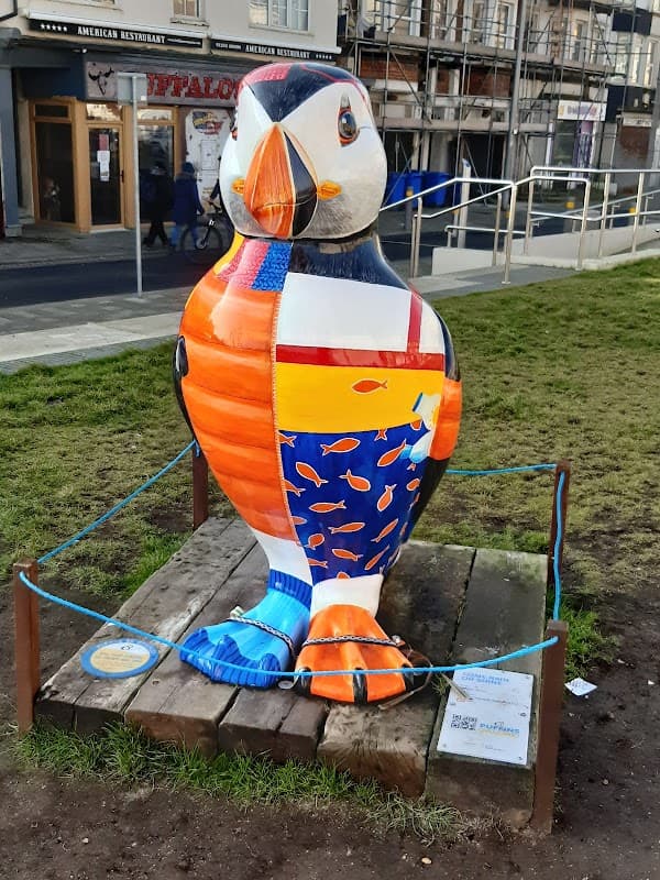 Colorful puffin statue with fish patterns, situated on grass near a pathway and buildings in Bridlington, Yorkshire.