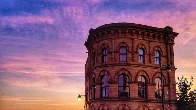 Historic stone building with rounded edges against a vibrant sunset sky in Batley, Yorkshire.
