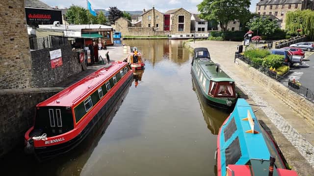 Colorful narrowboats docked along a calm waterway, with historic buildings and green trees in the background.