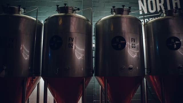 Three large metallic fermentation tanks with labels FV 01, FV 02, and FV 03, against a dark wall with "NORTH" text.