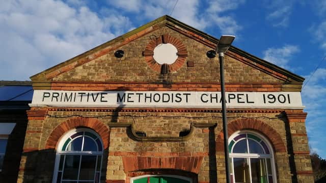 Historic brick building featuring "Primitive Methodist Chapel 1901" sign, with large windows and a clear blue sky.
