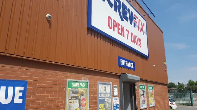Screwfix Sheffield storefront with a large sign, entrance door, and promotional posters on a sunny day.