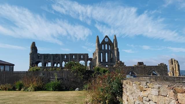 Whitby Holiday Cottages with lush greenery and the ruins of Whitby Abbey under a blue sky with scattered clouds.