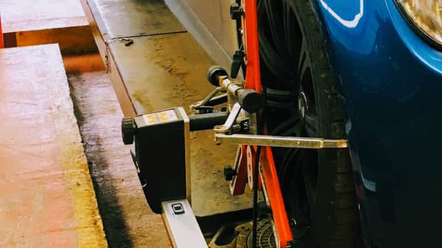 Blue car on a service ramp with wheel alignment equipment positioned near the front tire.