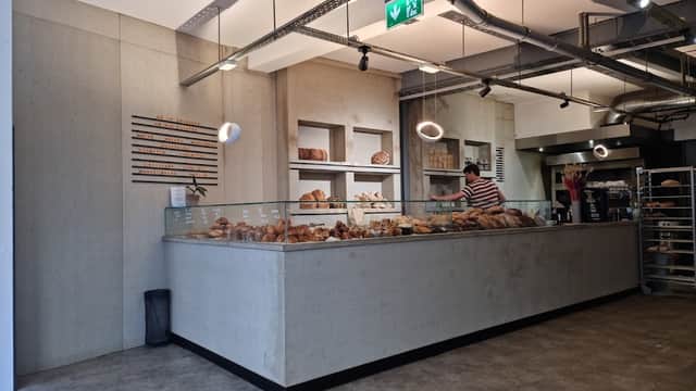 Modern bakery interior with a display of various breads, a staff member behind the counter, and minimalist decor.