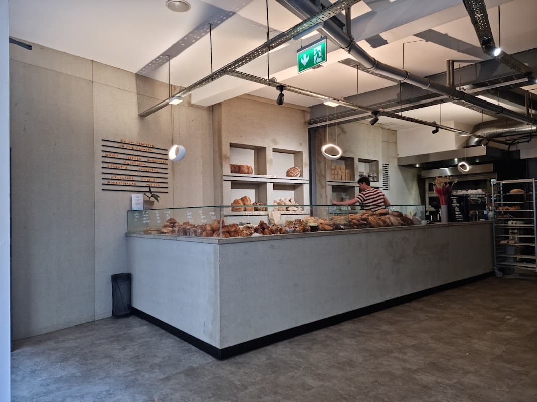 Modern bakery interior with a display of various breads, a staff member behind the counter, and minimalist decor.