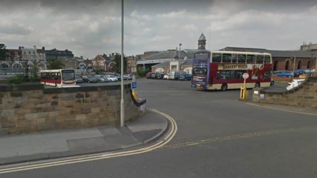 A busy car park in Scarborough with parked cars, a bus, and a mix of buildings in the background under a cloudy sky.