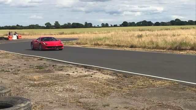 Red sports car on a racetrack surrounded by open fields and cloudy skies at Tockwith Motor Sports Centre.