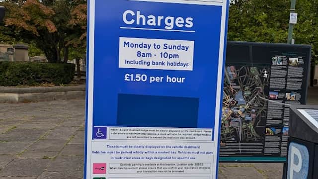Crown Court parking sign detailing charges and hours of operation, surrounded by trees and pavement.