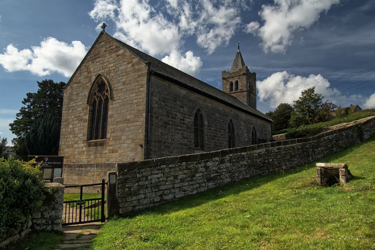 St Thomas' Church in Glaisdale, Yorkshire, features stone walls, a tall tower, and lush greenery surrounding it.