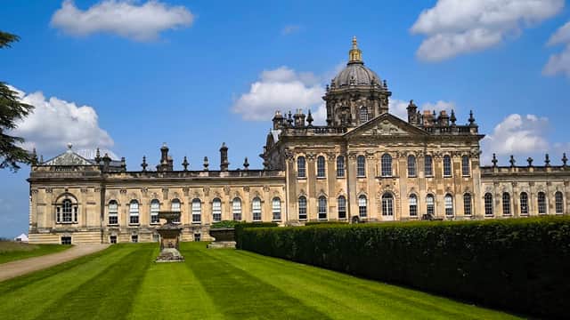 Historic grand building with ornate architecture, surrounded by lush green lawns and a clear blue sky.