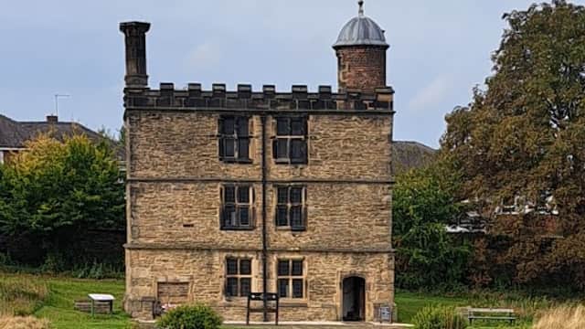 Historic stone building with a tower, surrounded by lush green lawn and flowering plants in Manor Lane Open Space.