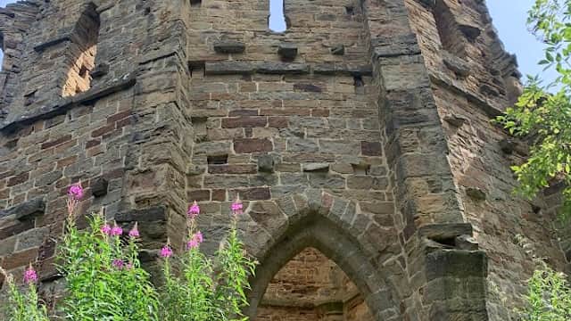 Ruins of a stone structure surrounded by greenery and wildflowers under a clear blue sky.