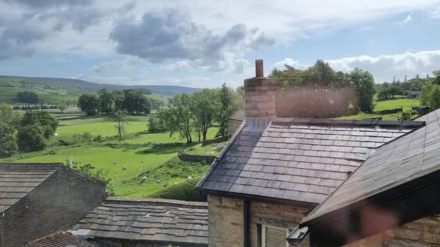 View of rolling green hills and trees from Ebor House, with a chimney and rooftops in the foreground.