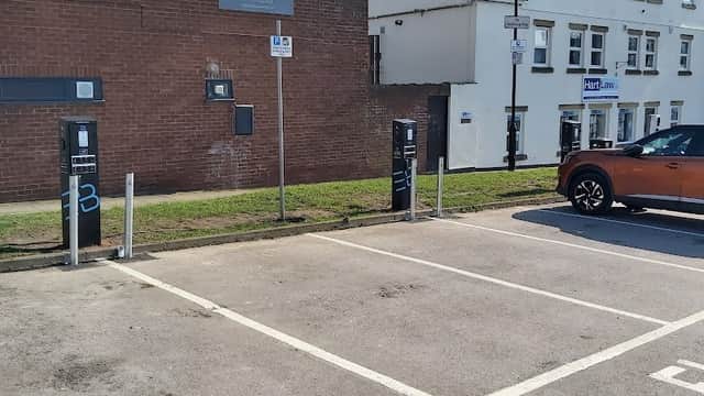 Free parking area with numbered spaces, adjacent buildings, and a parked orange car under clear blue skies.