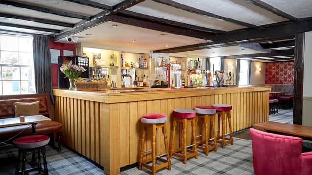 Warm wooden bar with stools, drinks on display, and cozy seating in a charming pub interior with patterned wallpaper.