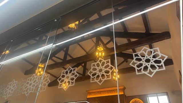 Intricate wooden beams and decorative lanterns reflect on a mirrored surface, with ornate patterns adorning the walls.