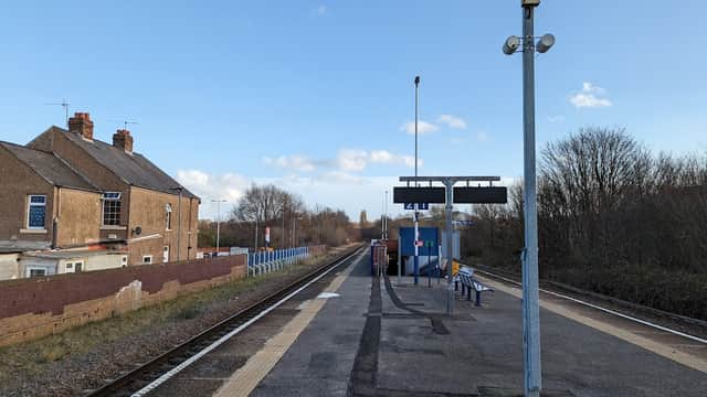 Bus stop at Darnall, Yorkshire, with a platform, benches, and buildings in a rural setting under a blue sky.