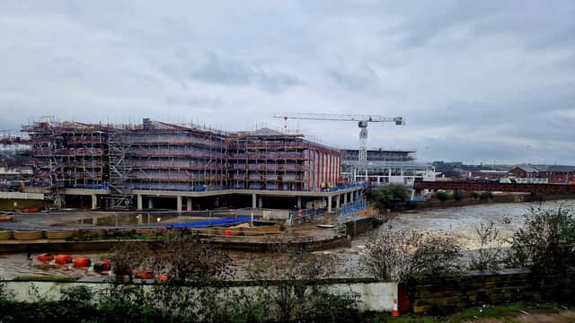 Construction site near a river, with scaffolding, cranes, and a cloudy sky in Rotherham, Yorkshire.