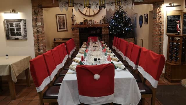 Long dining table set for a festive meal, with Santa hat chair covers and a decorated Christmas tree in the background.