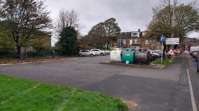 Empty car park with parked cars, green grass, and waste bins surrounded by trees and buildings in Bradford.