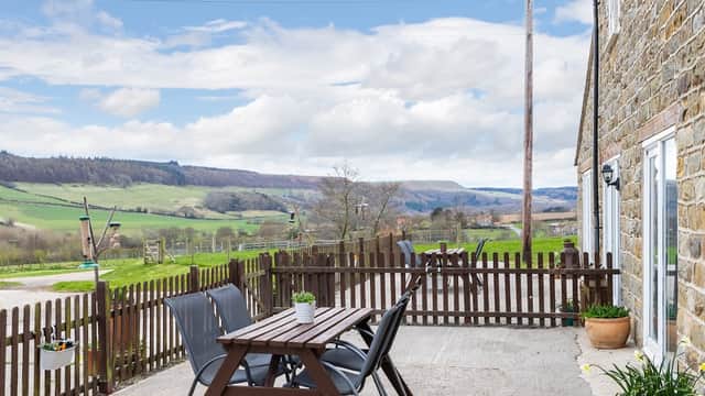 Outdoor seating area with wooden table and chairs, overlooking lush green hills and a cloudy sky in Harwood Dale.