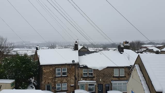 Snow-covered rooftops and streets in a residential area, with power lines and a cloudy sky in the background.
