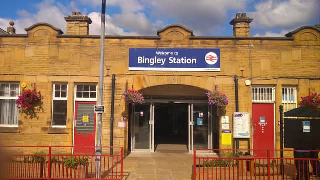 Welcome sign at Bingley Station, with red doors, flower baskets, and a clear blue sky.