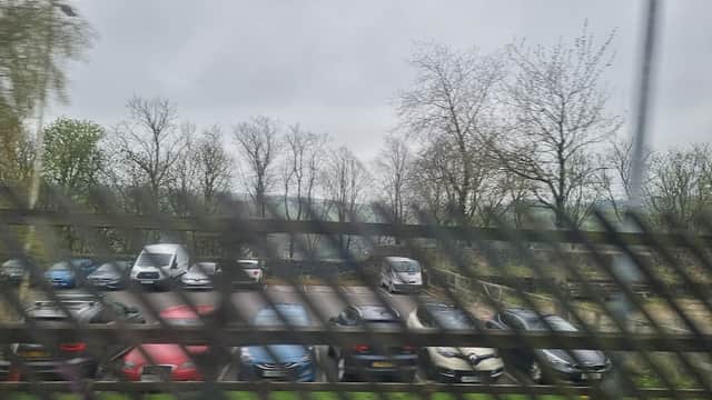 Car park filled with various vehicles surrounded by bare trees under a cloudy sky.