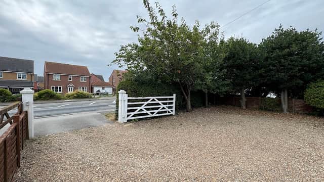 Gravel parking area with a white gate, surrounded by trees and houses under a cloudy sky in Skidby, Yorkshire.