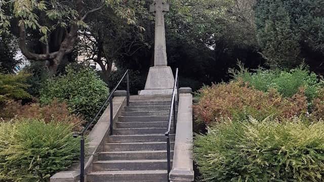 War memorial with a cross at the top of stone steps, surrounded by greenery in Denby Dale, Yorkshire.