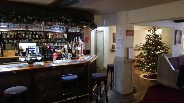 A cozy bar with a wooden counter, stools, festive decorations, and a Christmas tree in the background.