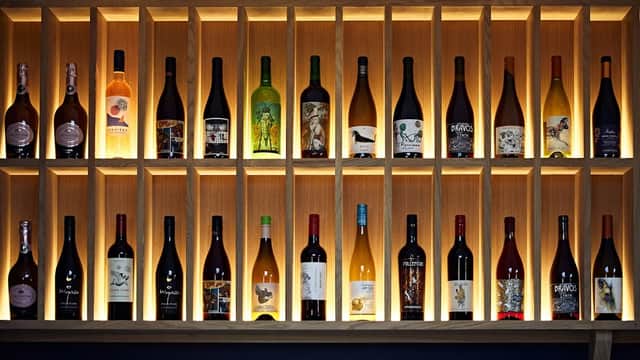 A wooden wine shelf displaying various bottles with unique labels, illuminated by soft lighting.