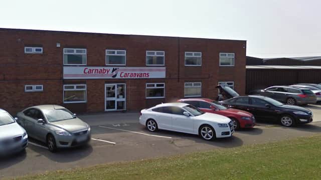 Carnaby Caravans Ltd building with a sign, parked cars, and a grassy area in front.