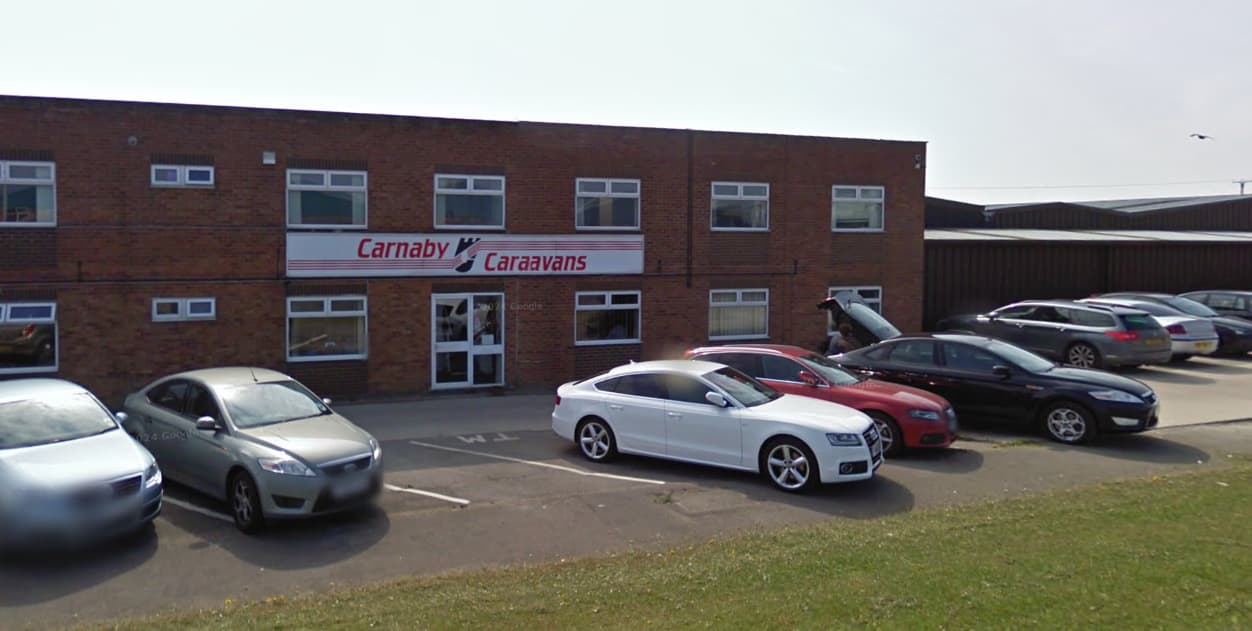 Carnaby Caravans Ltd building with a sign, parked cars, and a grassy area in front.