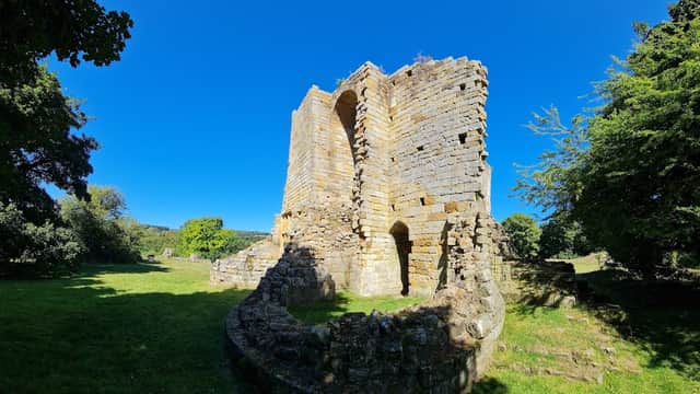 Ruins of Mulgrave Castle surrounded by lush greenery and a clear blue sky in Hutton Mulgrave, Yorkshire.