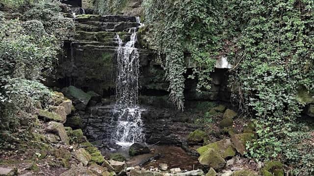 A serene waterfall cascading over moss-covered rocks, surrounded by lush greenery and trees in Wensley, Yorkshire.